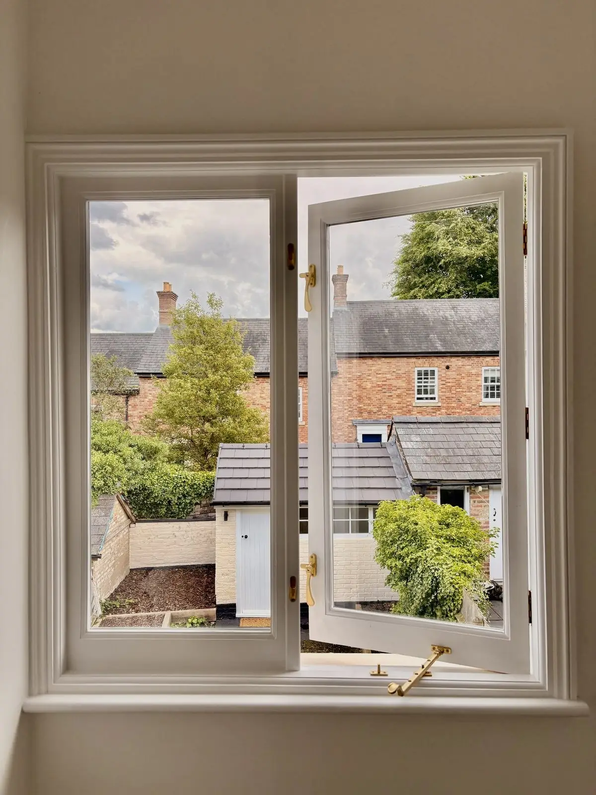 A white timber casement window open onto a garden