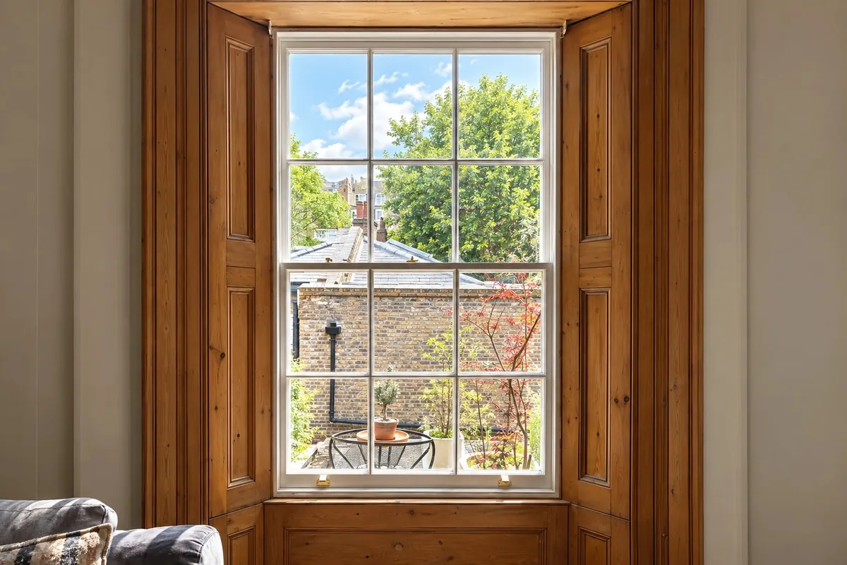 A six-over-six timber sash window between stripped pine panelled shutters, looking onto a garden
