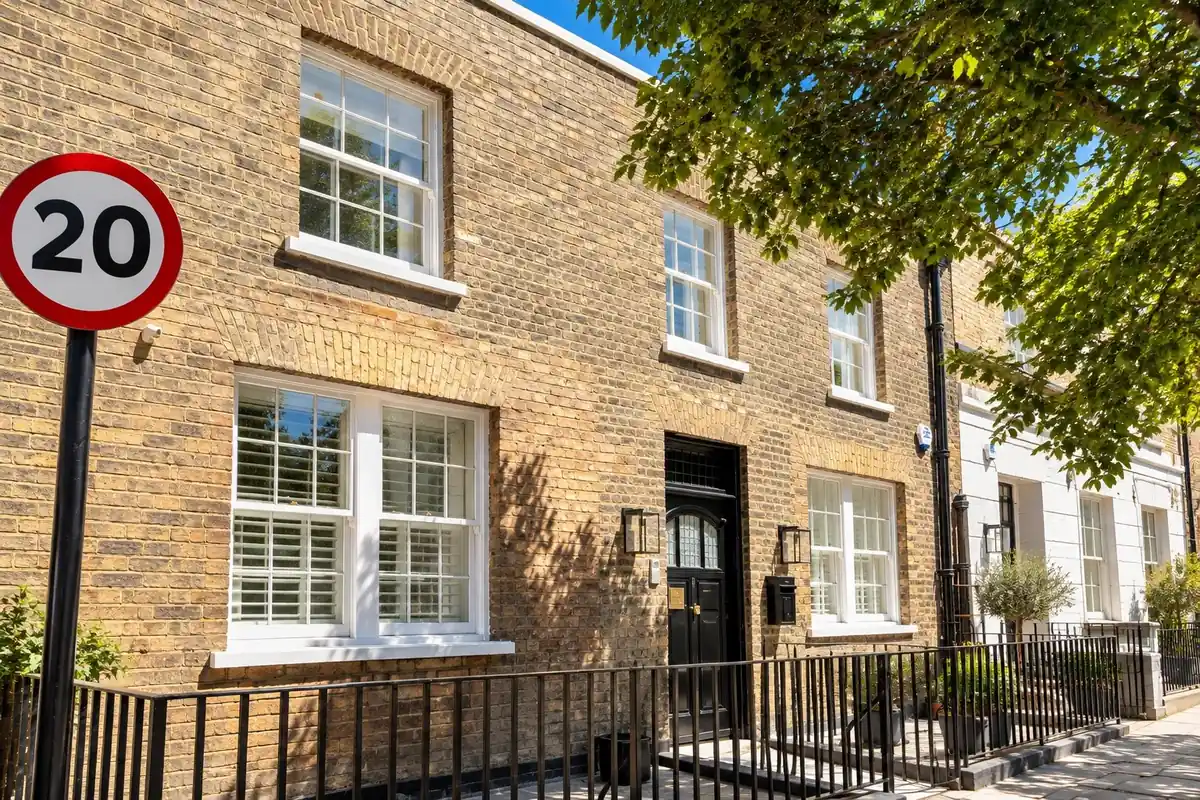 A London stock-brick terrace with white timber sash windows and a black front door behind railings