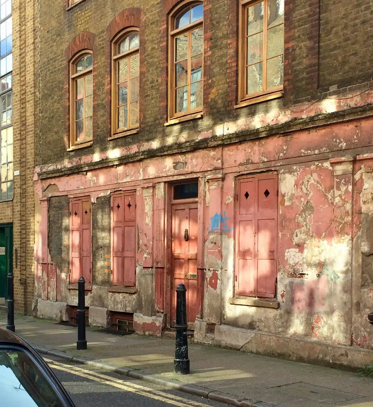 A weathered Georgian frontage with peeling pink render, painted shutters and a timber door
