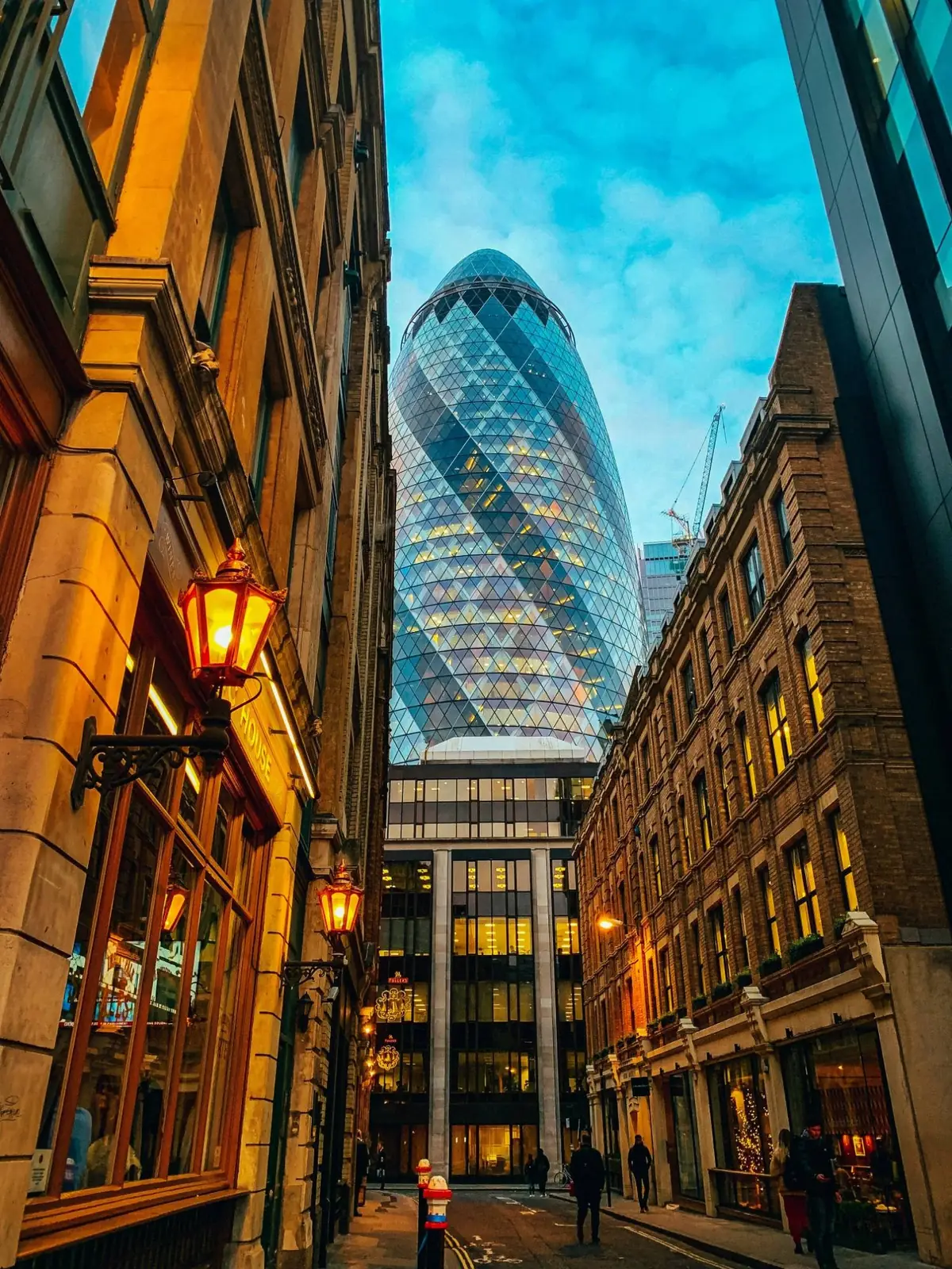 Victorian brick and stone commercial buildings with timber windows lining a City lane, with 30 St Mary Axe rising beyond