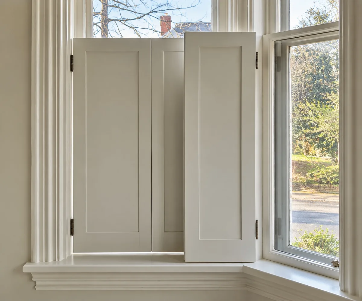 White panelled shutters folded back beside a timber sash window in a bay