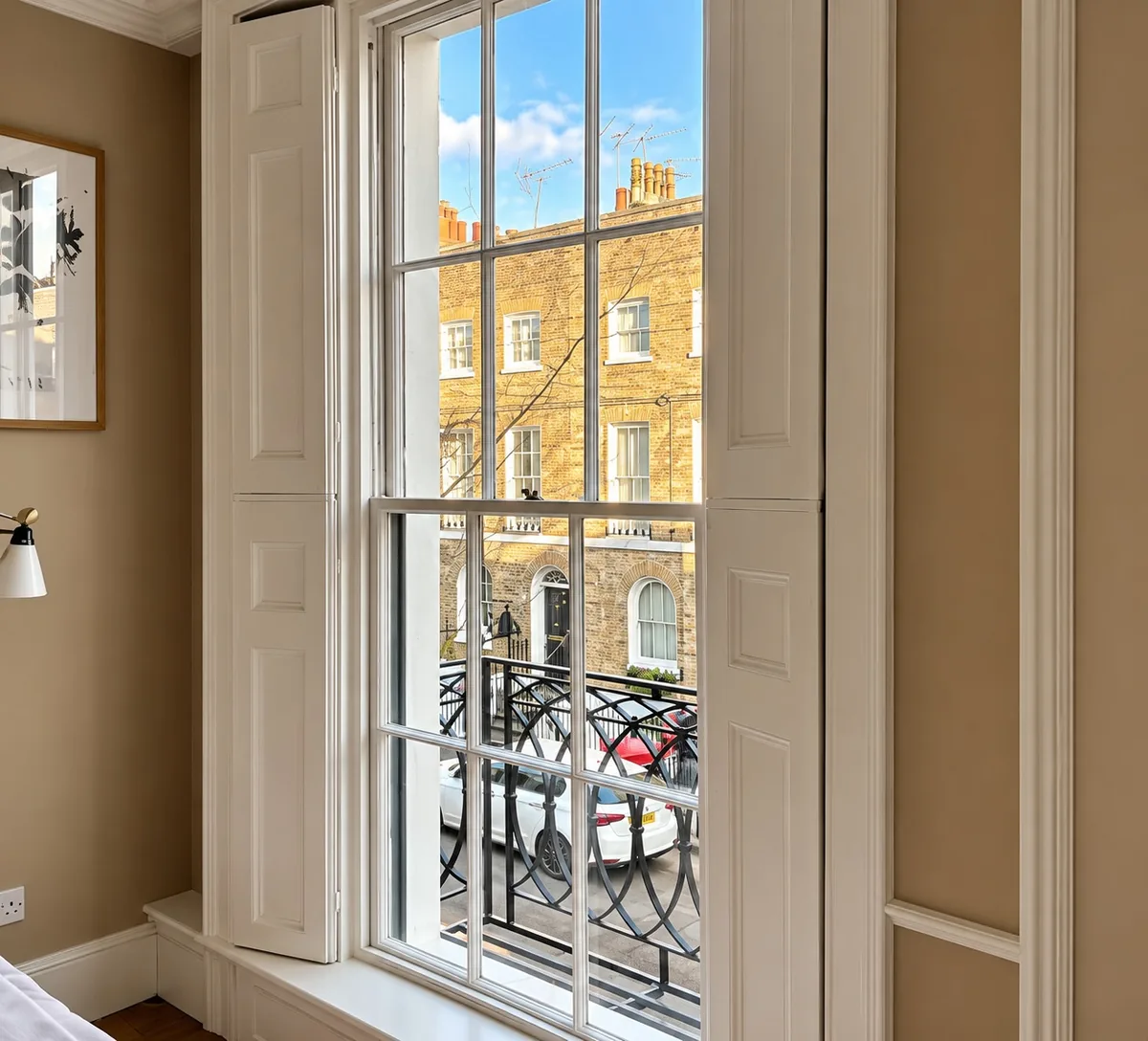 A tall timber sash window between folded shutters, looking out over a balcony to a Georgian terrace