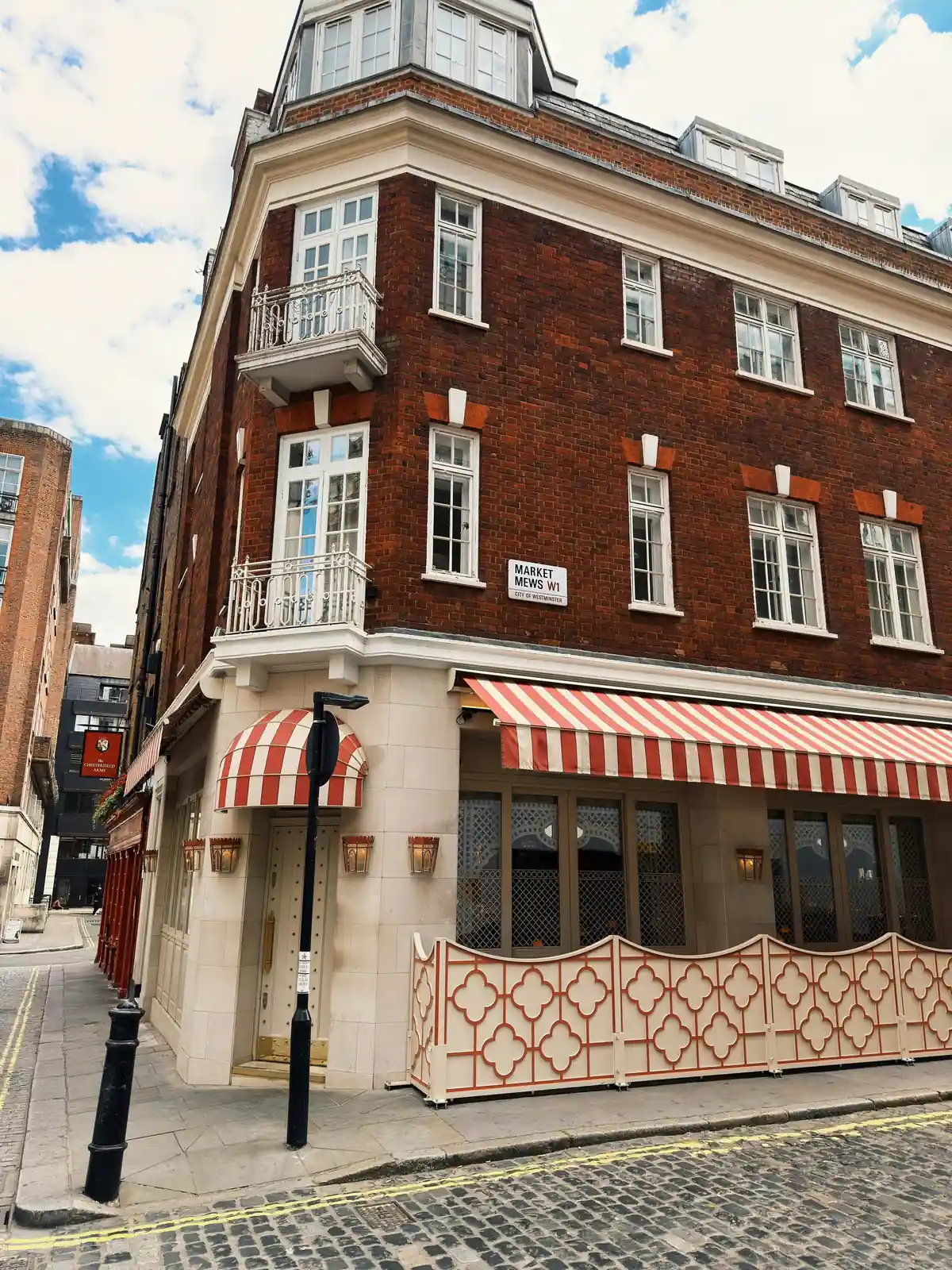 A red-brick corner building with white sash windows and striped awnings
