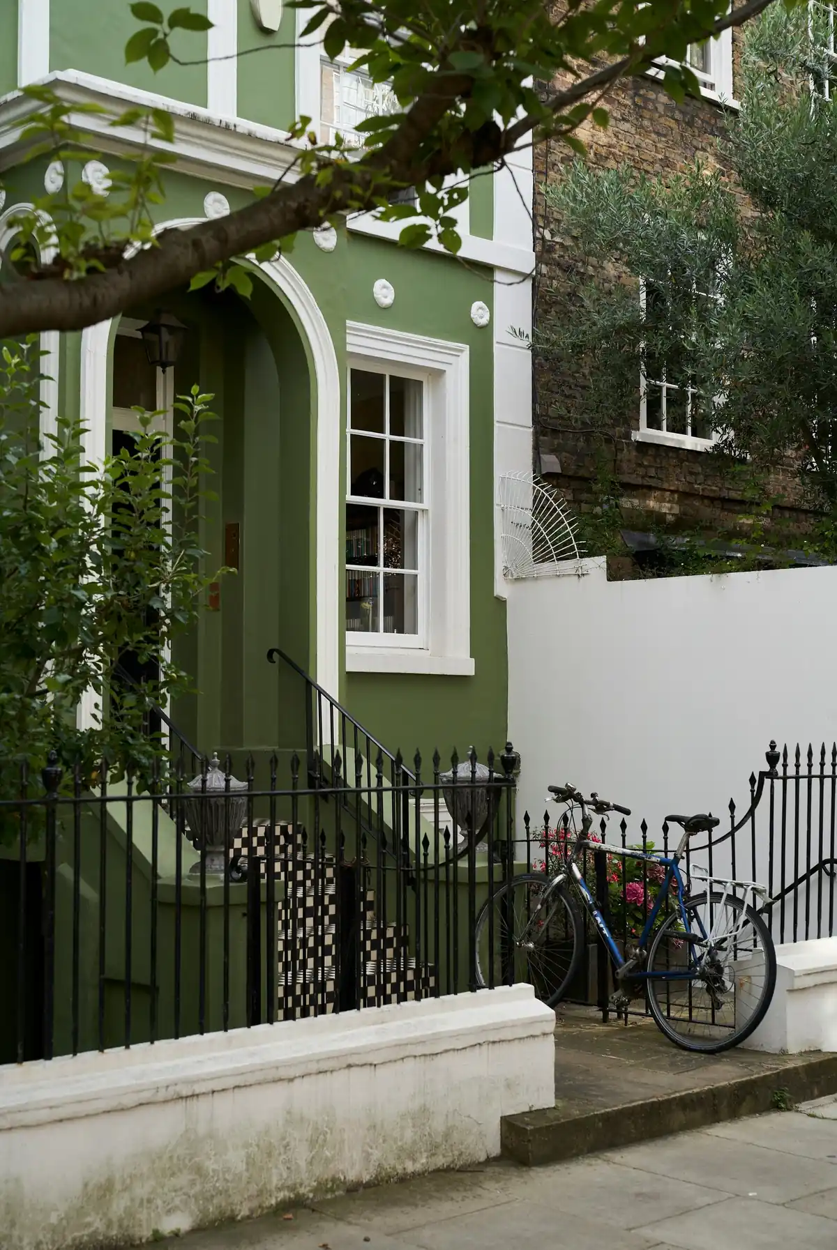 A green-painted stucco house with white surrounds, a six-over-six sash window and black railings