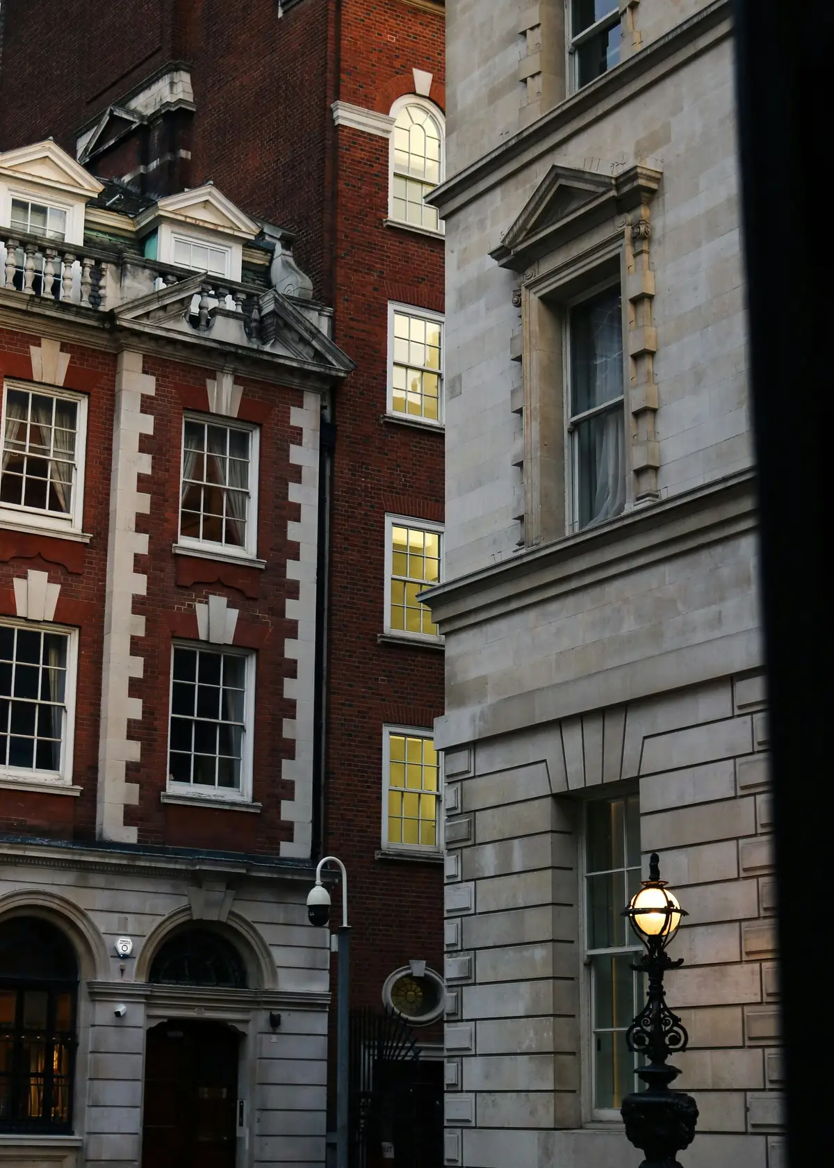 Red-brick and Portland stone buildings at dusk with lit sash windows