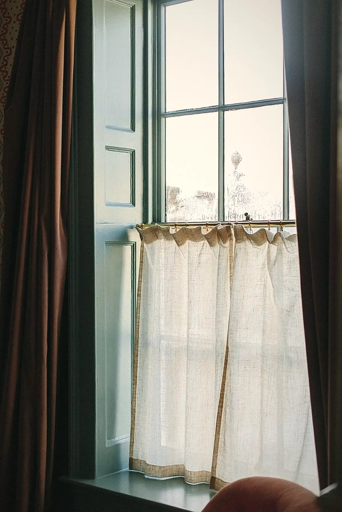 A sash window with folding panelled shutters and a linen café curtain