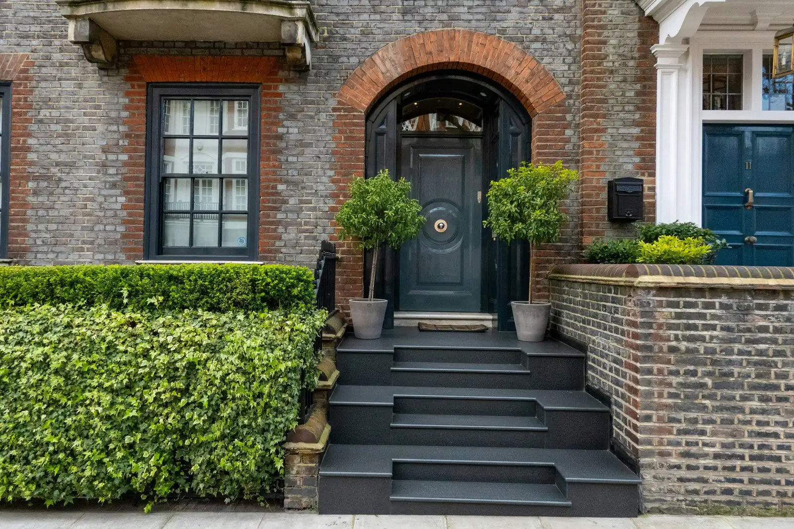 A brick house with an arched black front door, stone steps and Georgian-bar sash windows