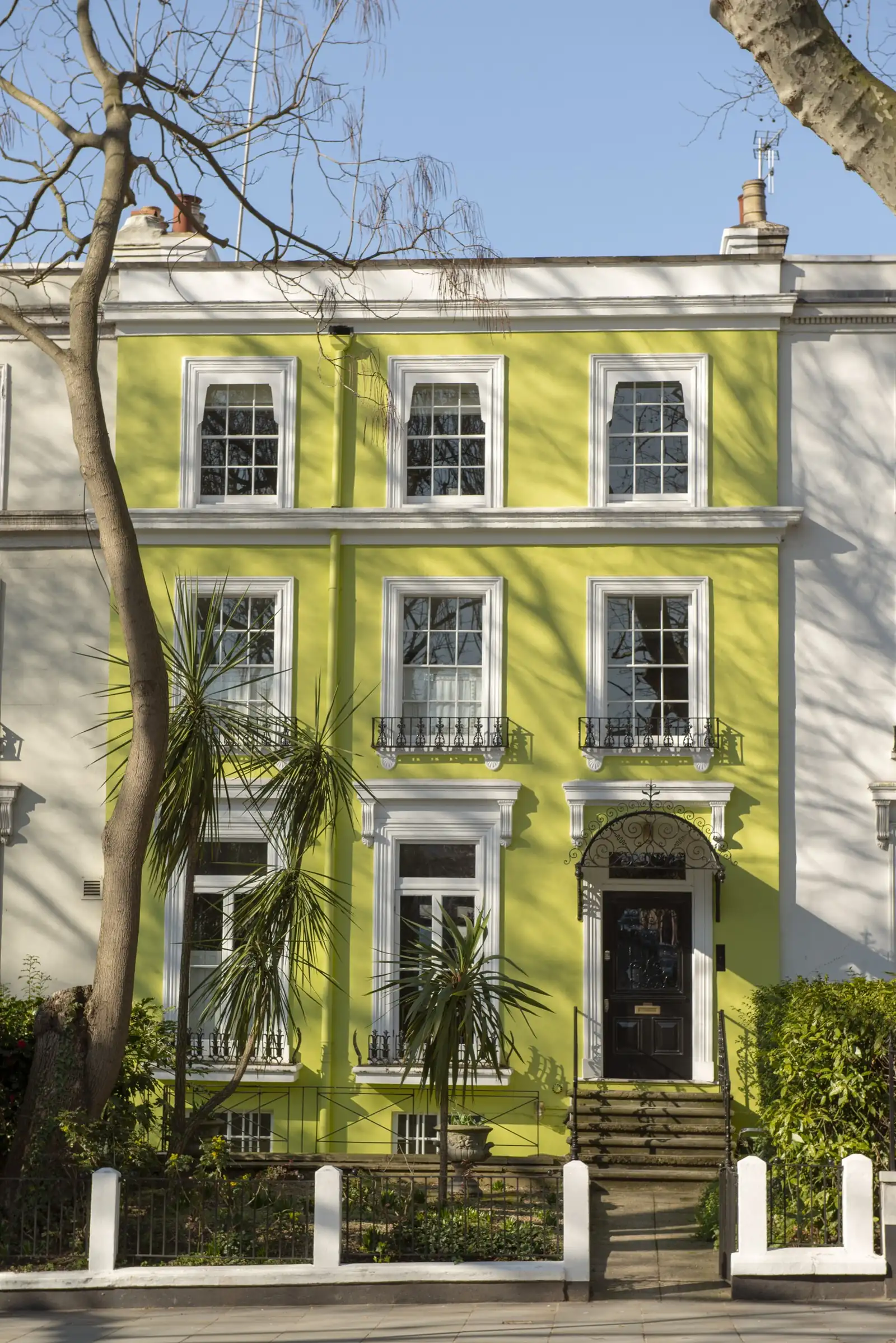 A lime-green stucco terraced house with white-framed six-over-six sash windows, cast-iron balconettes and a black panelled front door