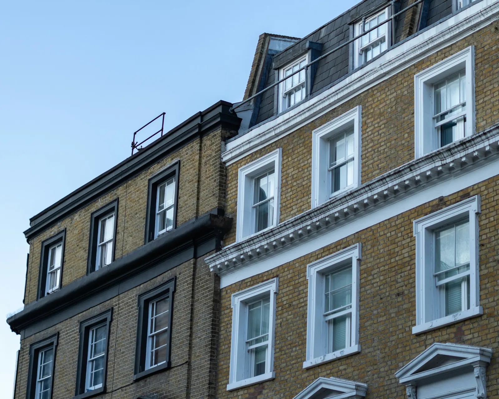 Upper storeys of two London stock-brick buildings with white and dark-framed sash windows