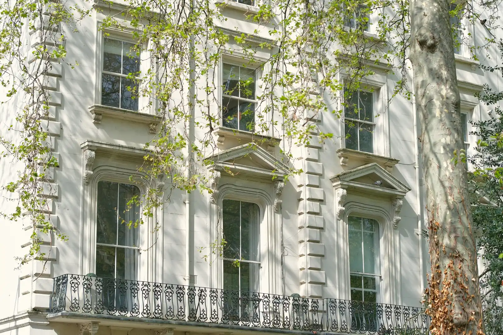A white stucco Italianate terrace with tall sash windows and pedimented architraves