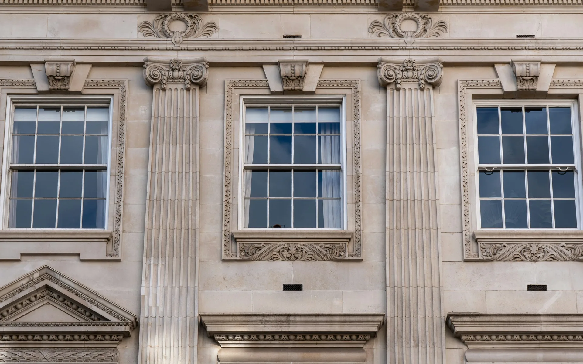 A Portland stone facade with Georgian-bar sash windows, fluted pilasters and pedimented surrounds