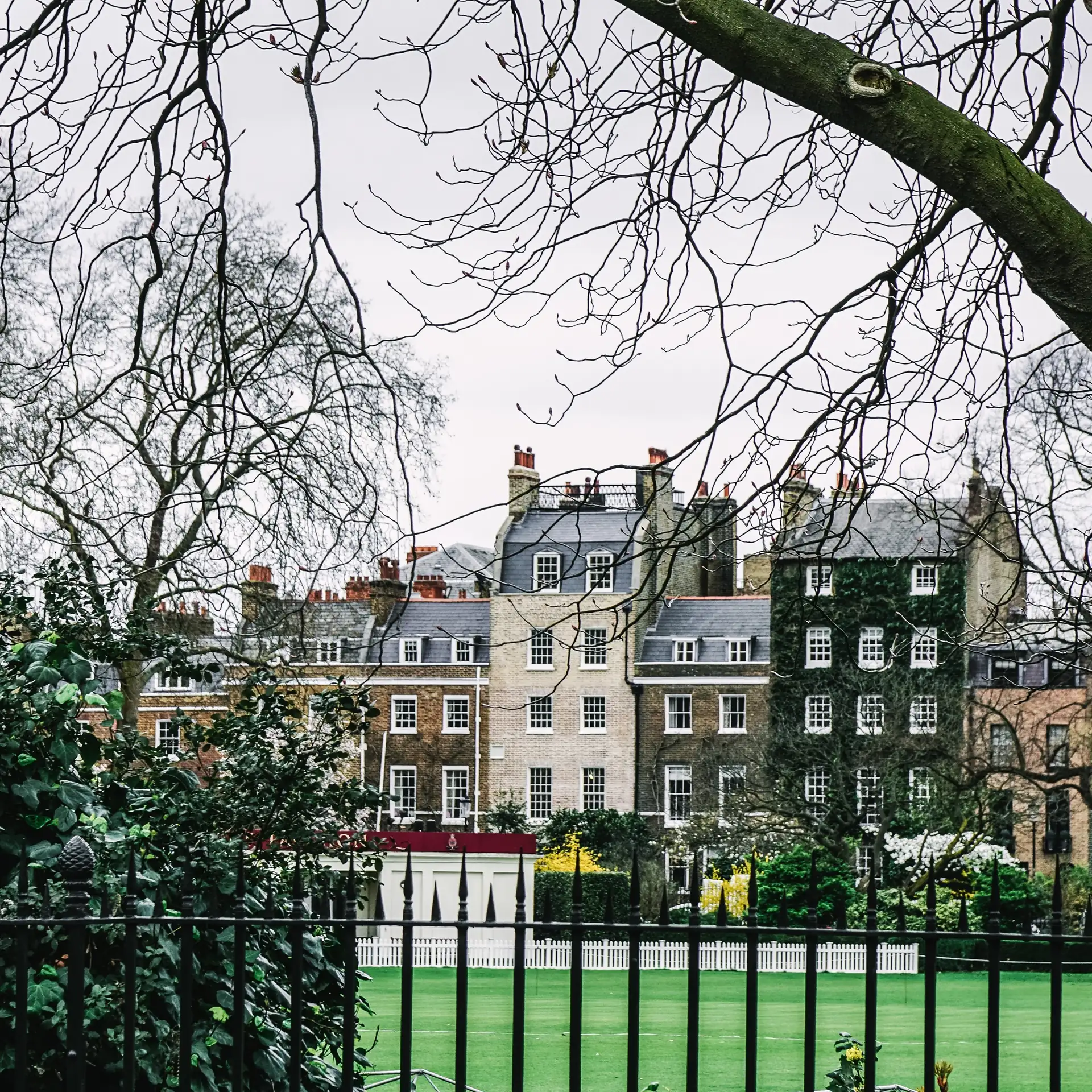 Early Georgian brick houses with tall small-paned sash windows and mansard roofs, seen across a garden through railings