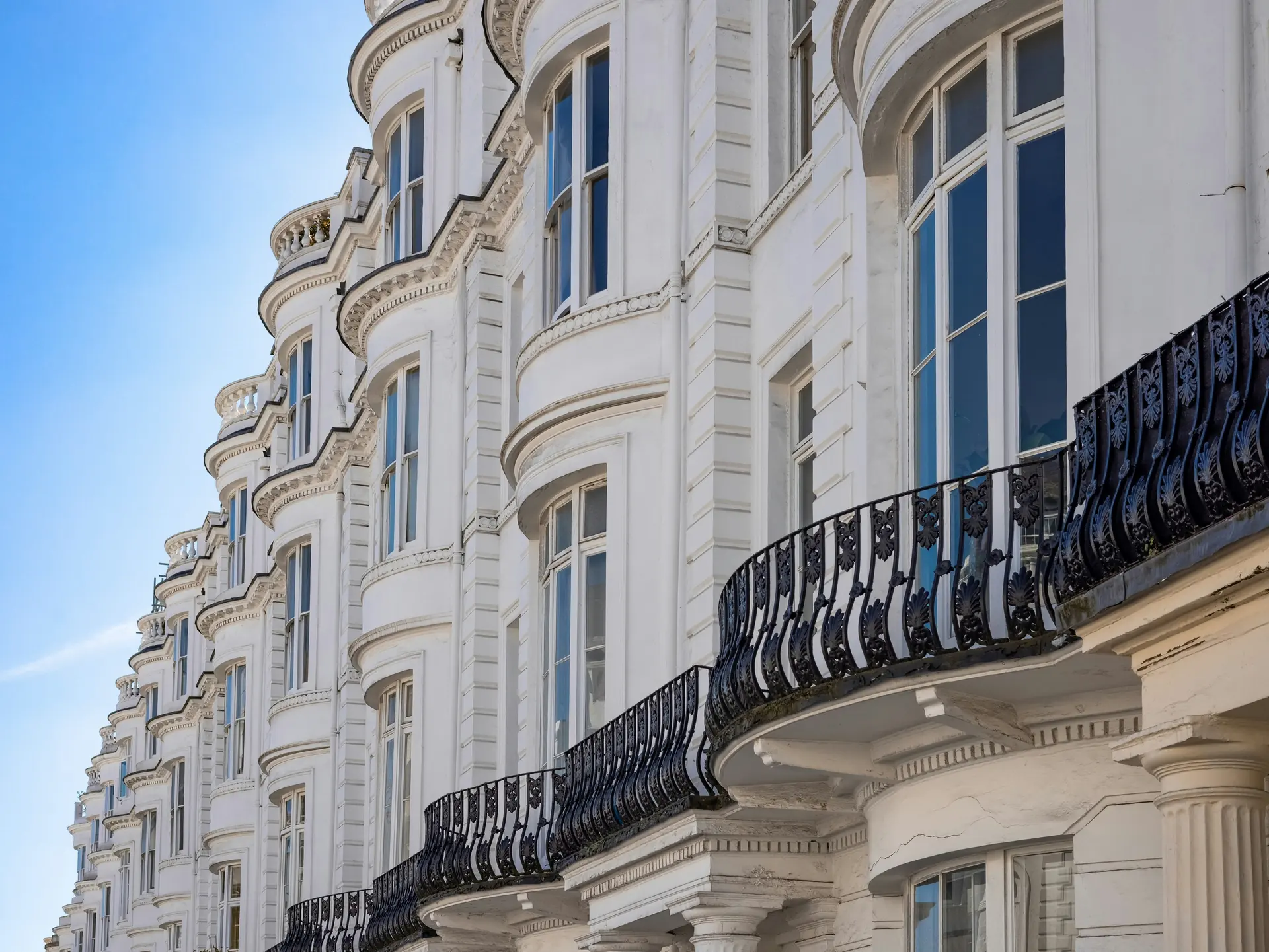 A long run of white stucco terraced houses with stacked bow windows and curved cast-iron balconies