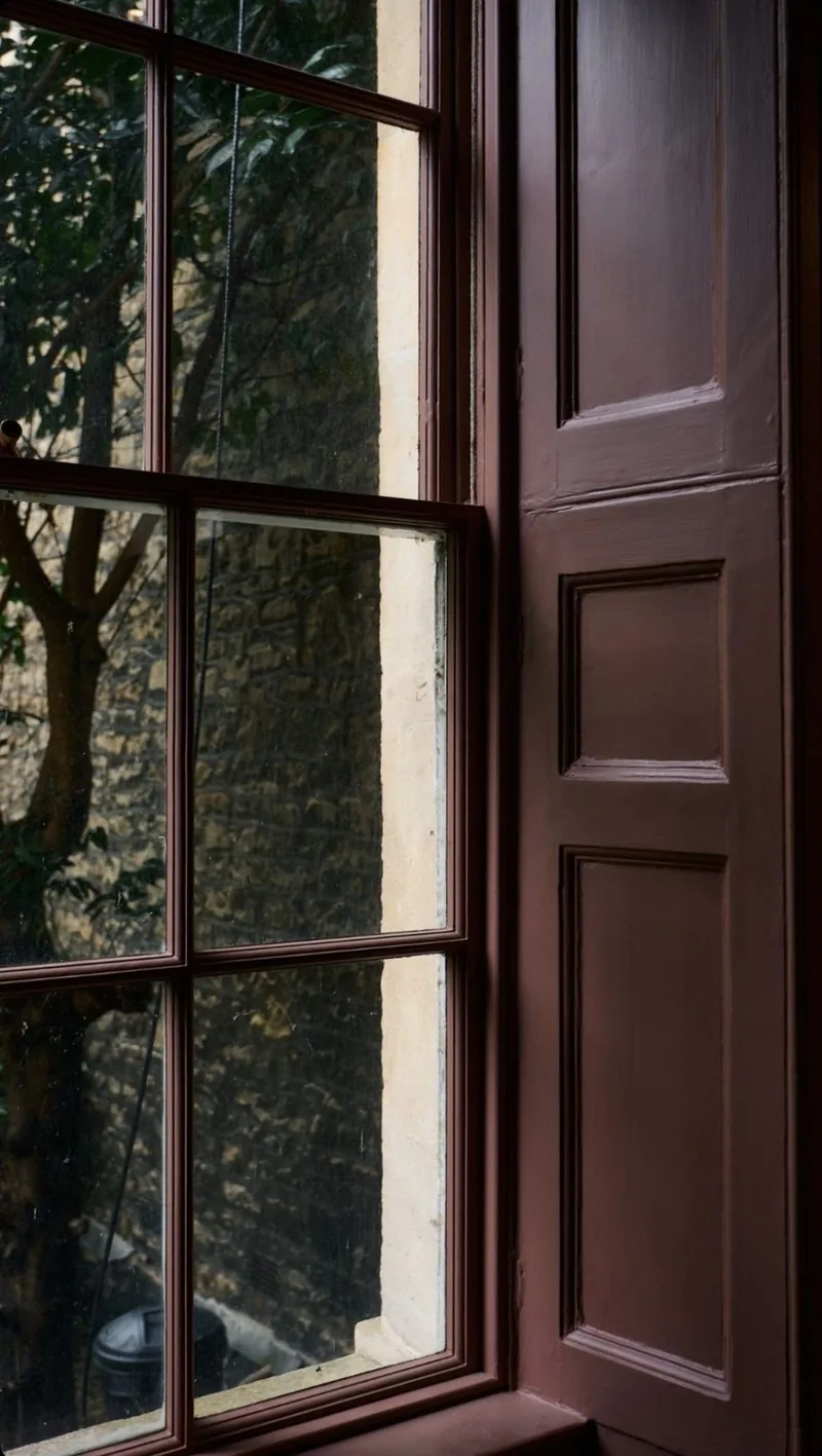 A small-paned sash window beside a dark-painted panelled shutter