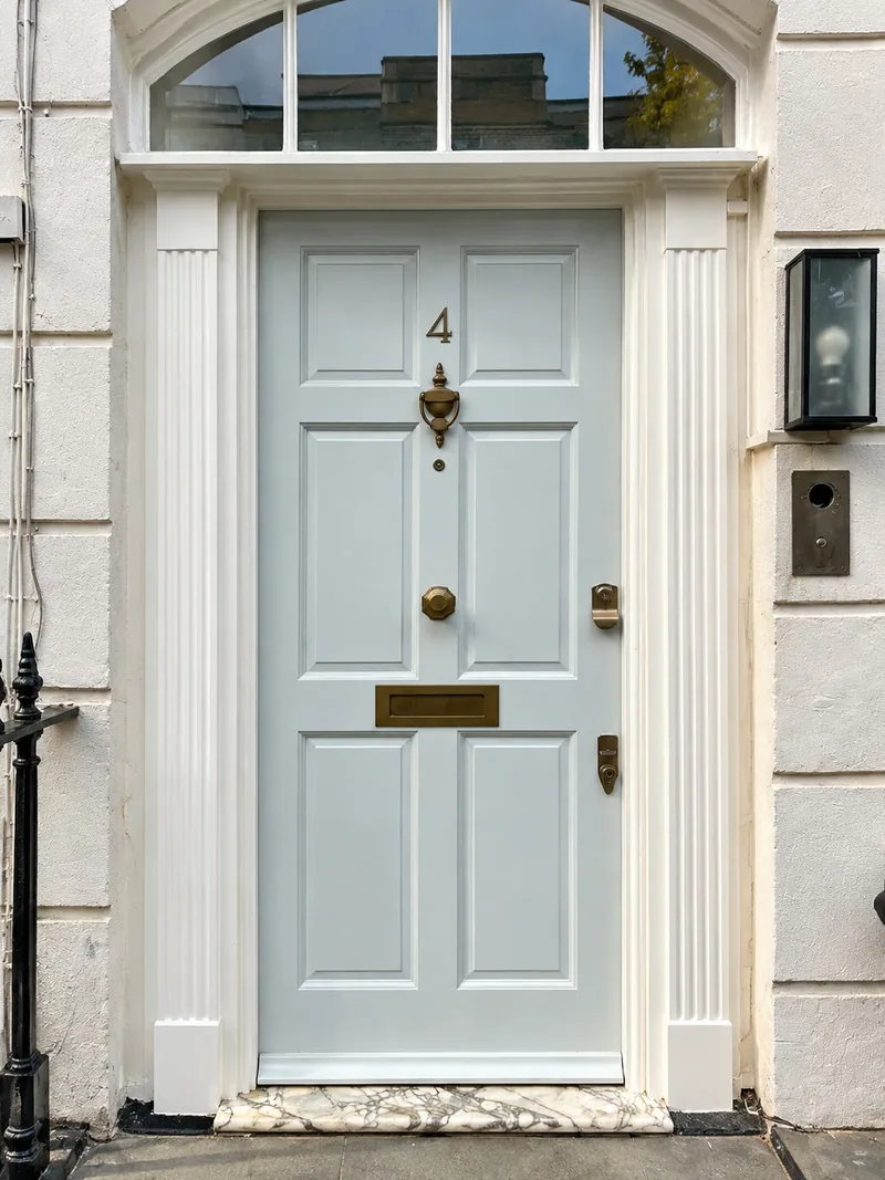 A six-panel front door with a fanlight above, repaired and hand-painted pale blue, in a white stucco doorcase with fluted pilasters