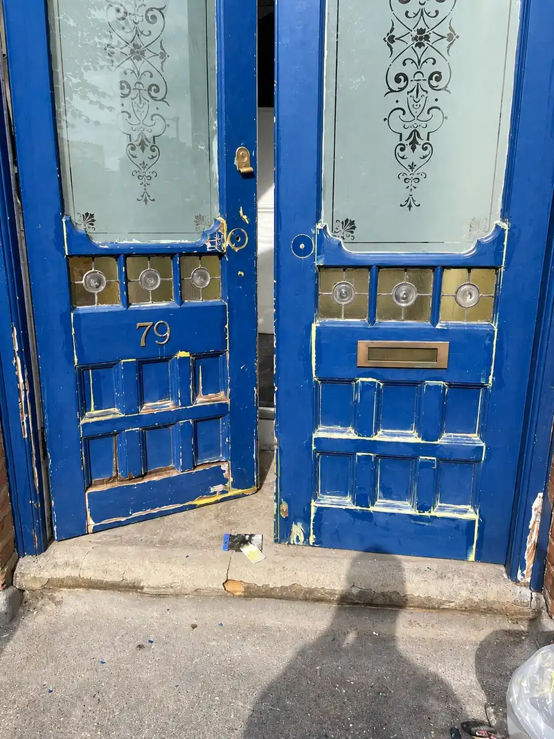 The same doors before the work, with flaking blue paint and worn bottom rails