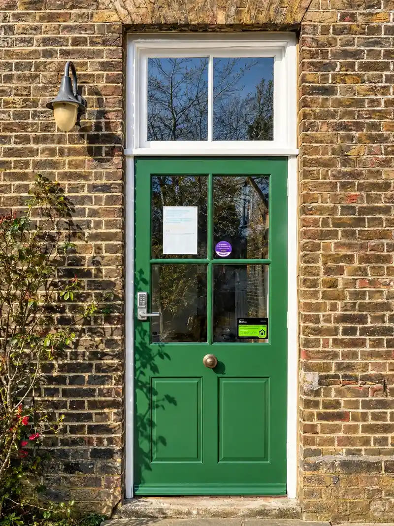 A half-glazed timber door in a brick wall, restored and repainted bright green, with a fanlight above